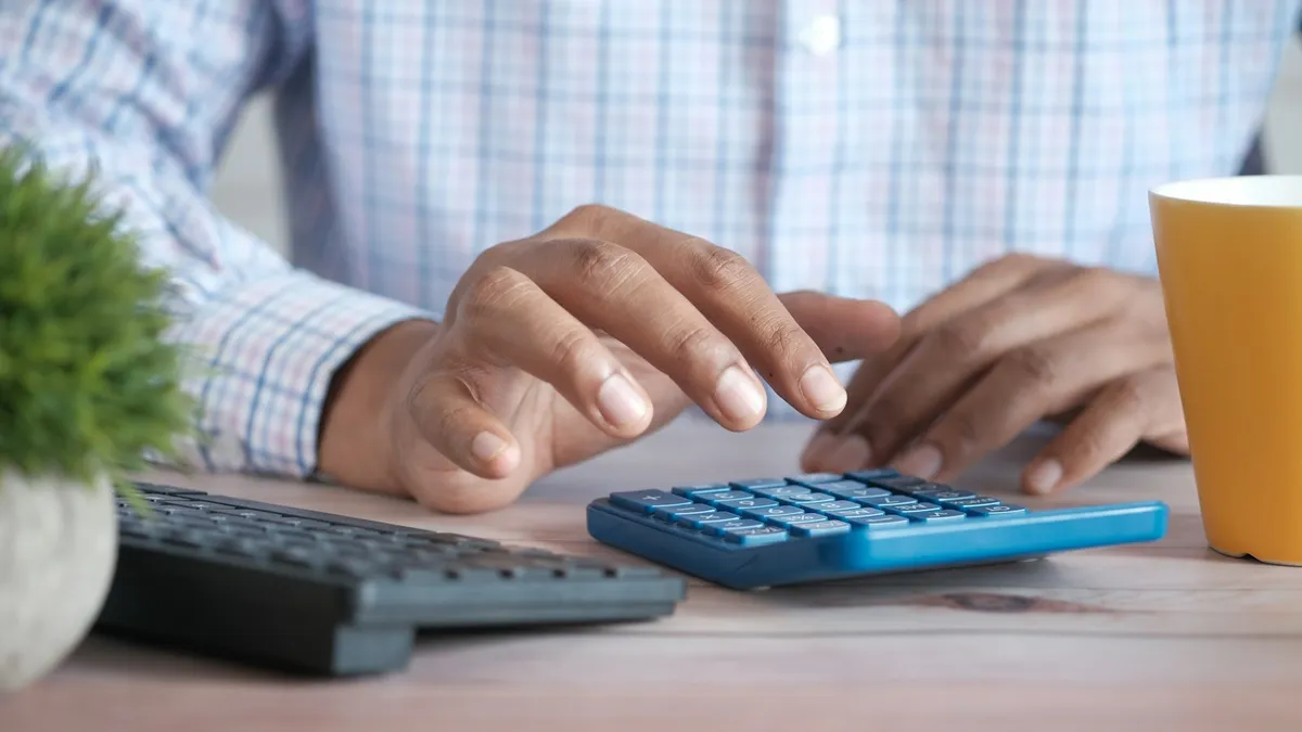 Hands working out numbers on a blue calculator at a desk
