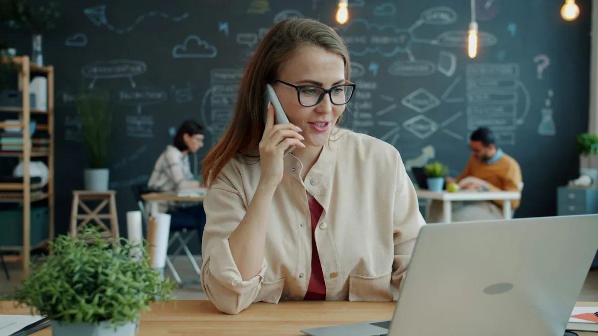 A smiling woman on a phone call while working at a laptop